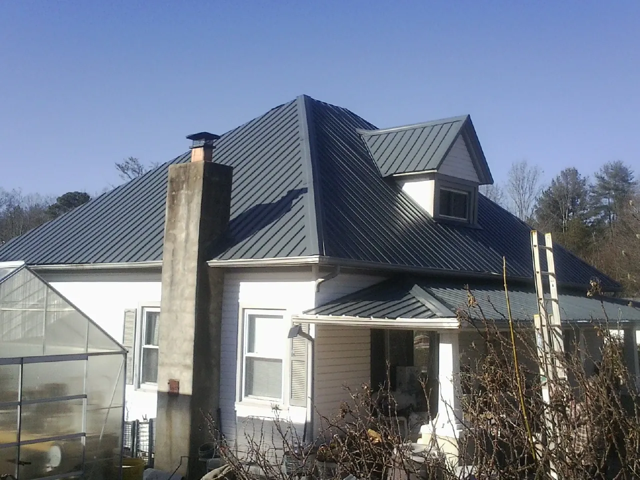 Dark blue standing seam metal roof on a white farmhouse with dormer — Slate & Tile Roof Repair by Roofing Brothers in Columbus